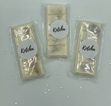 Load image into Gallery viewer, The picture is of a wax melt in the shape of a chocolate bar. The colour is white with gold and silver biodegradable glitter wrapped in plastic with the brand name &quot;Kotcha&quot; on it. There are crystals surrounding the image and a white background.
