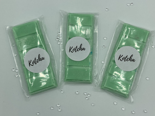 The picture is of a wax melt in the shape of a chocolate bar. The colour is green with silver biodegradable glitter wrapped in plastic with the brand name 