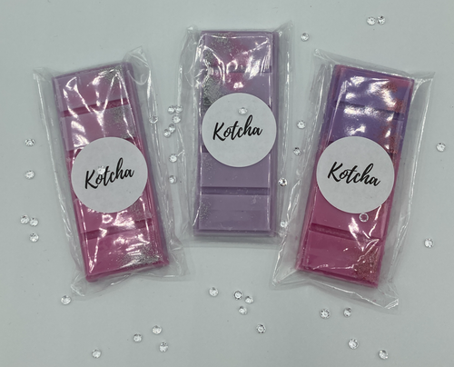 The picture is of a wax melt in the shape of a chocolate bar. The colour is purple with silver biodegradable glitter wrapped in plastic with the brand name 